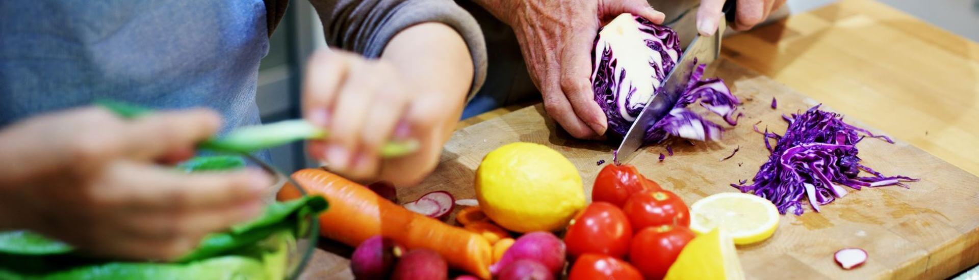 two people chopping assorted vegetables on a cutting board